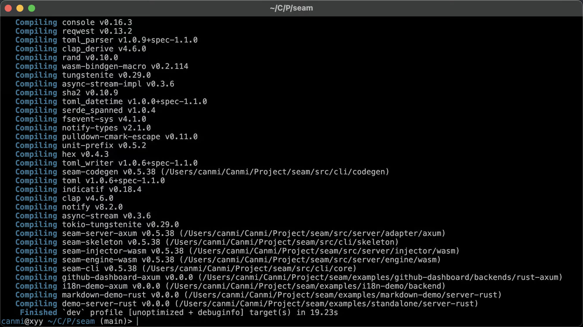 一张 macOS 终端截图，标题为 `~/C/P/seam`，显示一次成功 Cargo 构建的末尾部分：约三十行青色的 "Compiling" 输出向上滚动，先是第三方 crate（console v0.16.3、reqwest v0.13.2、clap v4.6.0、tokio-tungstenite v0.29.0、notify v8.2.0、wasm-bindgen-macro v0.2.114），最后是 v0.5.38 的本地 workspace 成员——seam-codegen、seam-server-axum、seam-skeleton、seam-injector-wasm、seam-engine-wasm 和 seam-cli——其后是 `examples/` 目录下四个 v0.0.0 的示例 crate（github-dashboard rust-axum backend、i18n-demo backend、markdown-demo server-rust、standalone server-rust）。最后一行是 `Finished \`dev\` profile [unoptimized + debuginfo] target(s) in 19.23s`，提示符回到 `canmi@xyy ~/C/P/seam (main)>`。它证明 seam workspace——一个拆分为 CLI、server-adapter、codegen 和 WASM engine/injector crate 以及若干示例后端的 Rust 项目——在 `main` 分支上能够干净地完成构建，用时约二十秒。